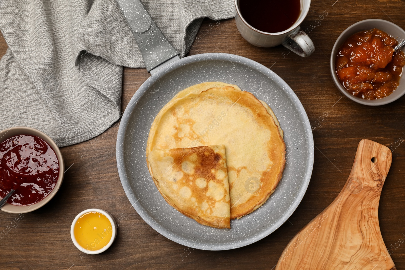 Photo of Frying pan with delicious crepes, jams, honey and aromatic tea on wooden table, flat lay
