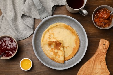 Photo of Frying pan with delicious crepes, jams, honey and aromatic tea on wooden table, flat lay