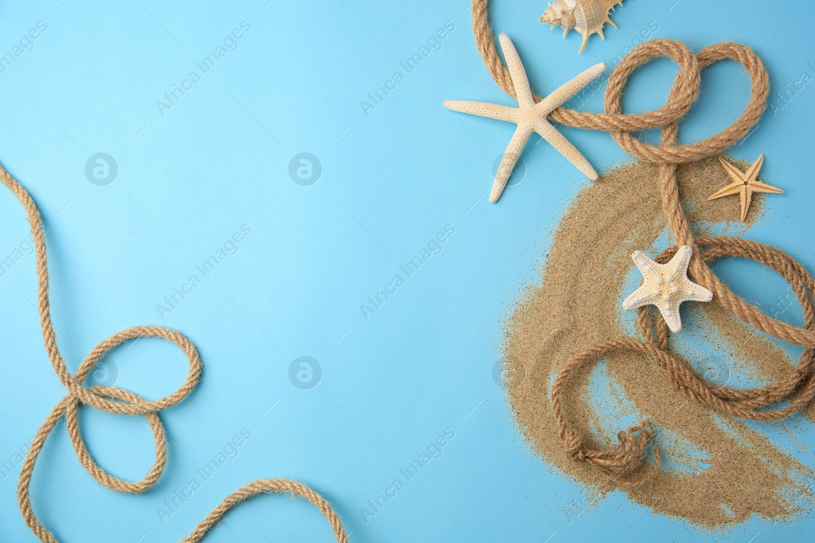 Photo of Beautiful sea stars, rope and sand on light blue background, flat lay. Space for text