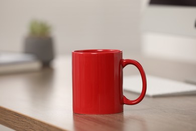 Photo of Red ceramic mug on wooden table at workplace