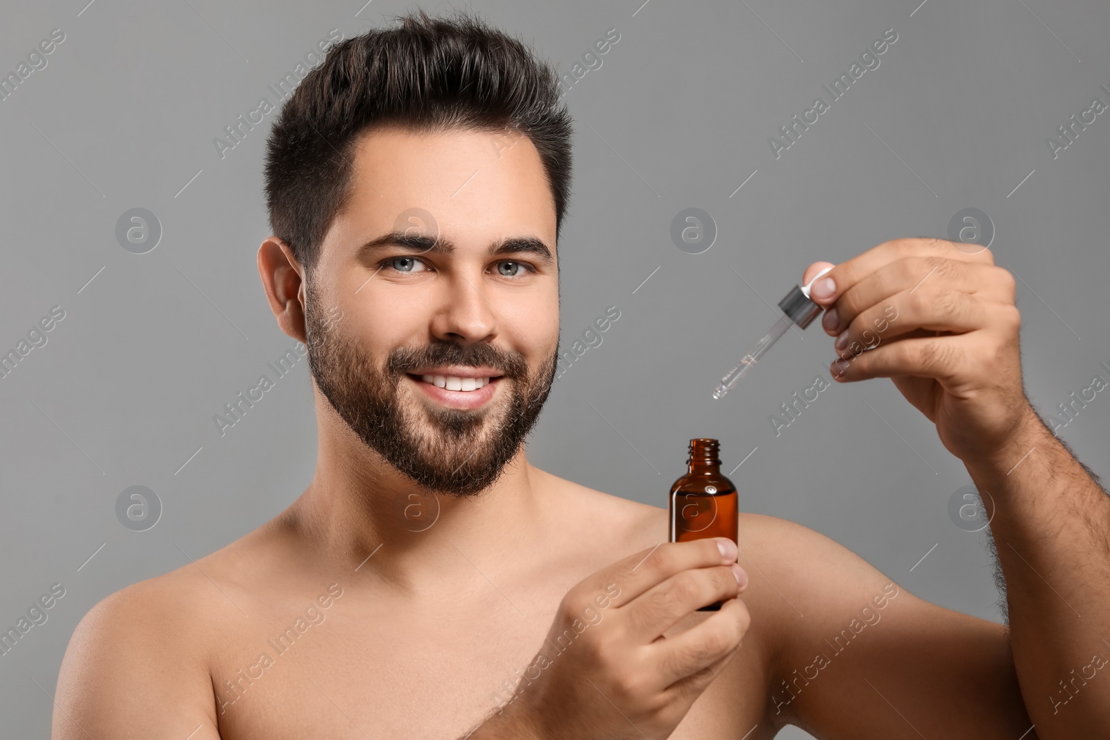 Photo of Handsome man with cosmetic serum in hands on grey background