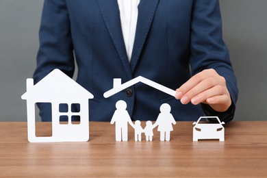 Photo of Woman with cutout paper family, house and car at table, closeup. Life insurance concept
