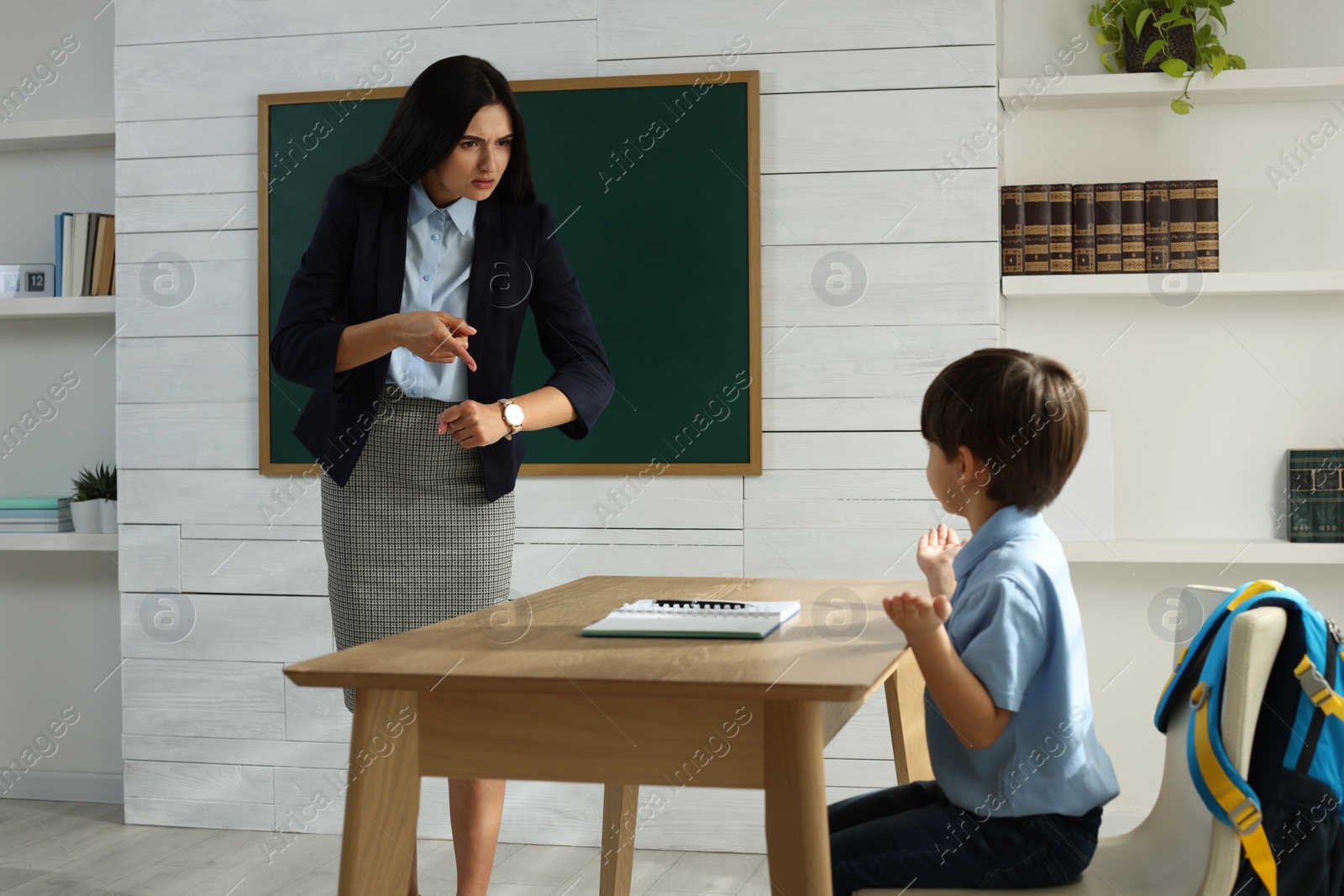 Photo of Teacher pointing on wrist watch while scolding pupil for being late in classroom