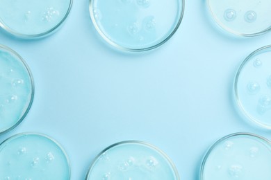 Photo of Frame of Petri dishes with liquid samples on light blue background, flat lay. Space for text