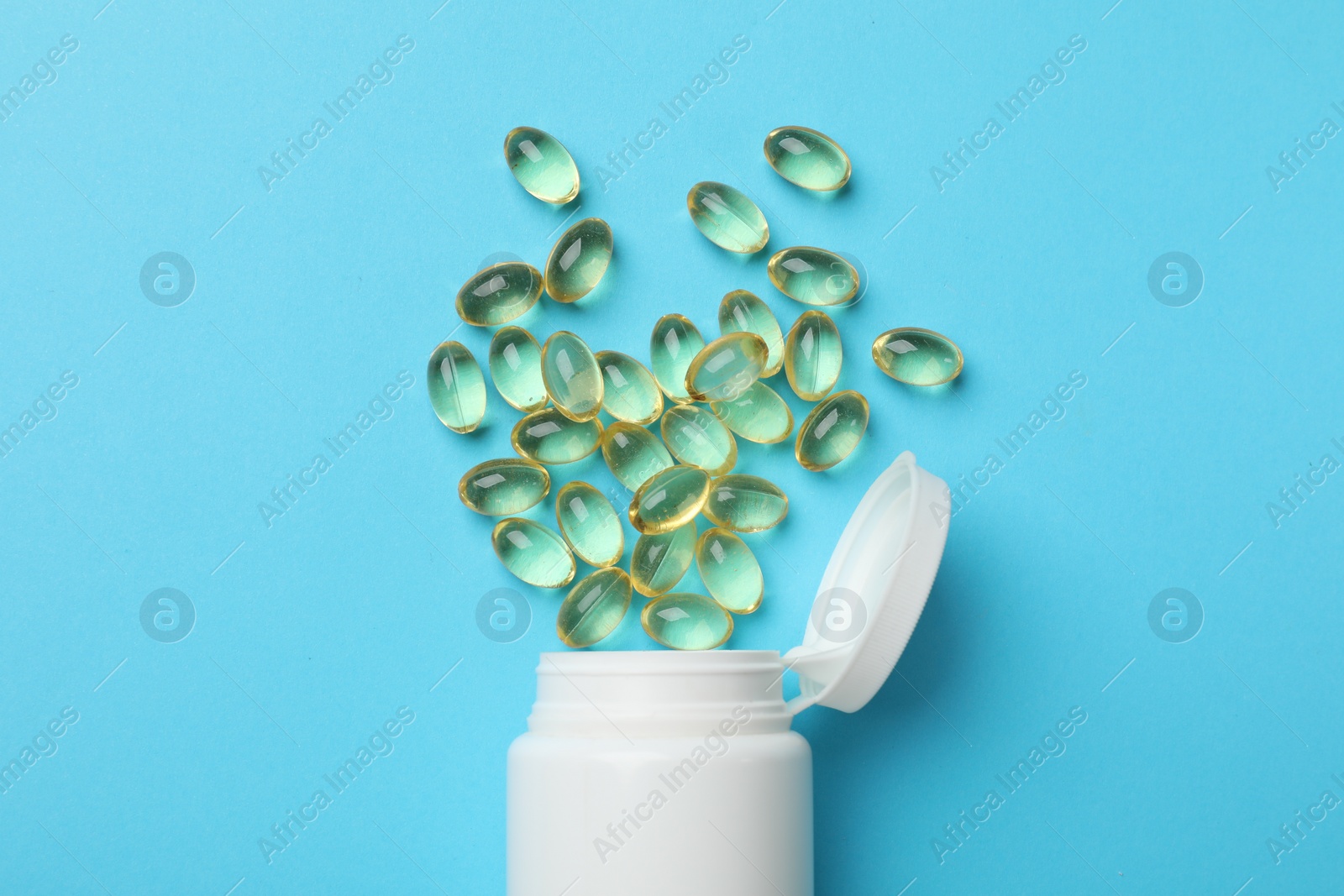 Photo of White bottle and different vitamin capsules on light blue background, top view