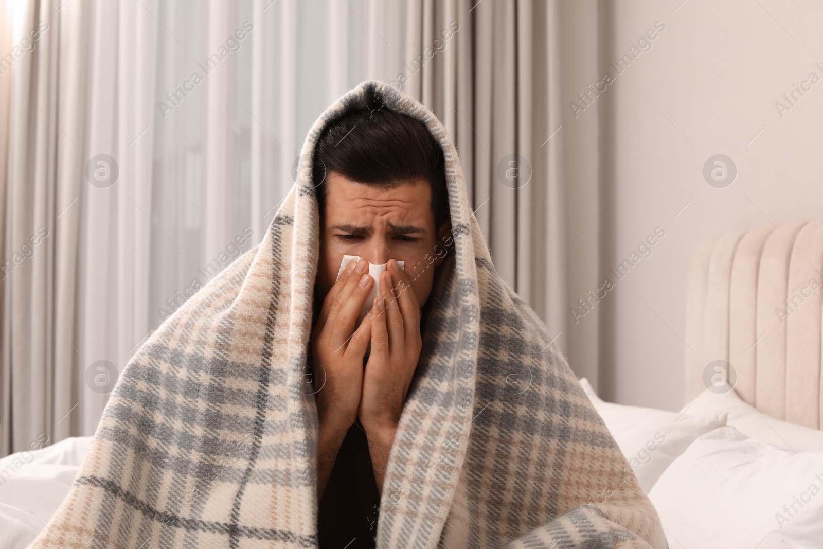 Photo of Sick man with tissue suffering from cold on bed at home