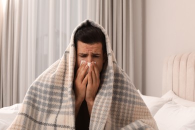 Sick man with tissue suffering from cold on bed at home
