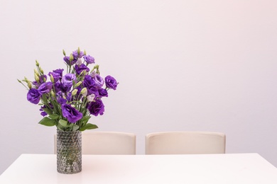 Photo of Vase with beautiful flowers on white table against color background. Stylish interior