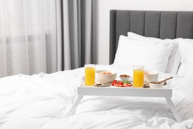 Photo of Tasty breakfast served in bed. Oatmeal, juice, fruits, almonds and honey on tray, space for text