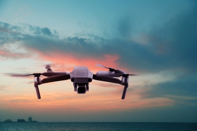 Image of Modern drone flying over sea at sunset. Aerial survey