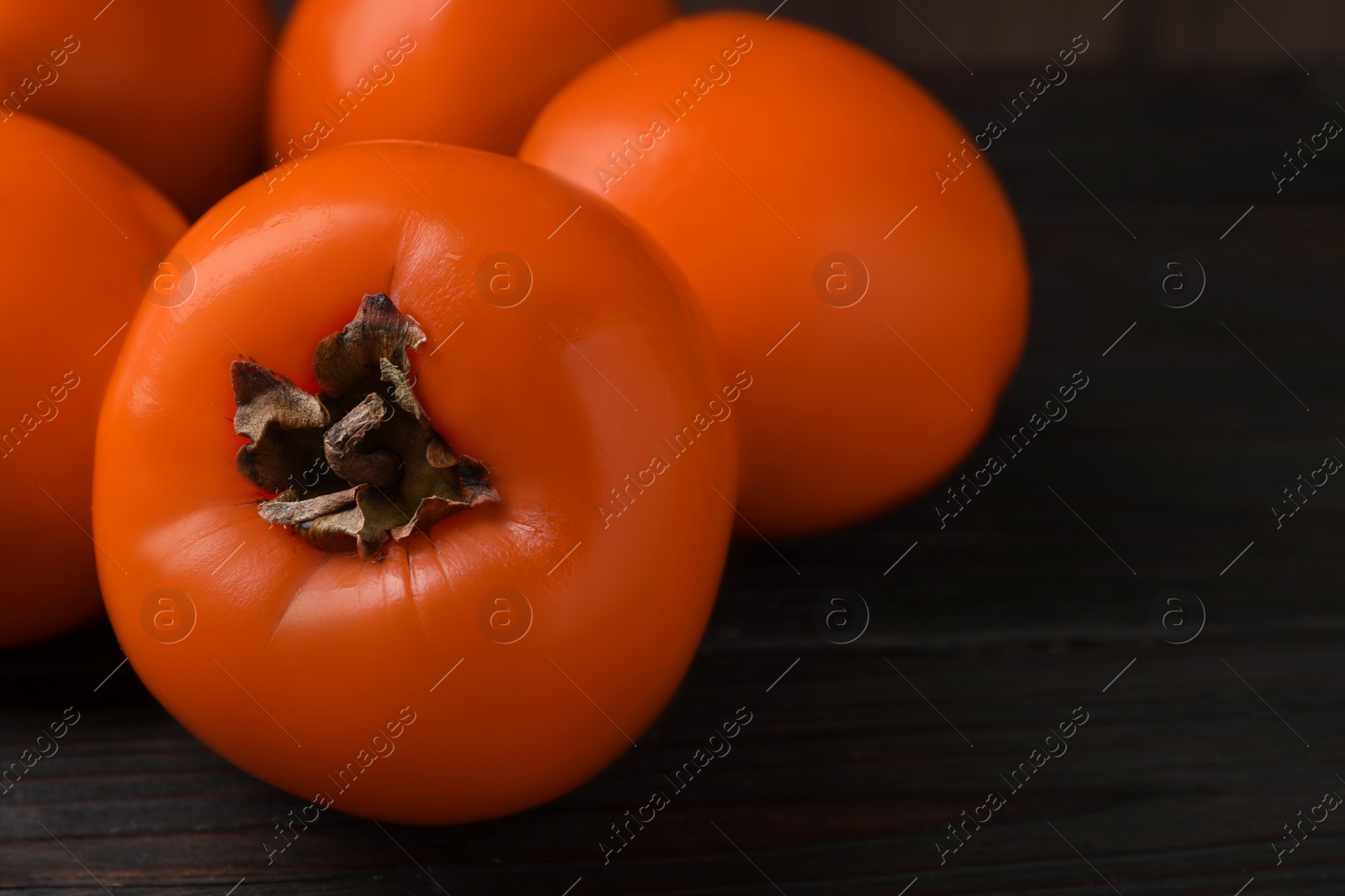 Photo of Delicious ripe persimmons on dark wooden table, closeup