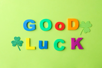 Photo of Phrase GOOD LUCK made of color letters and clover leaves on green background, flat lay