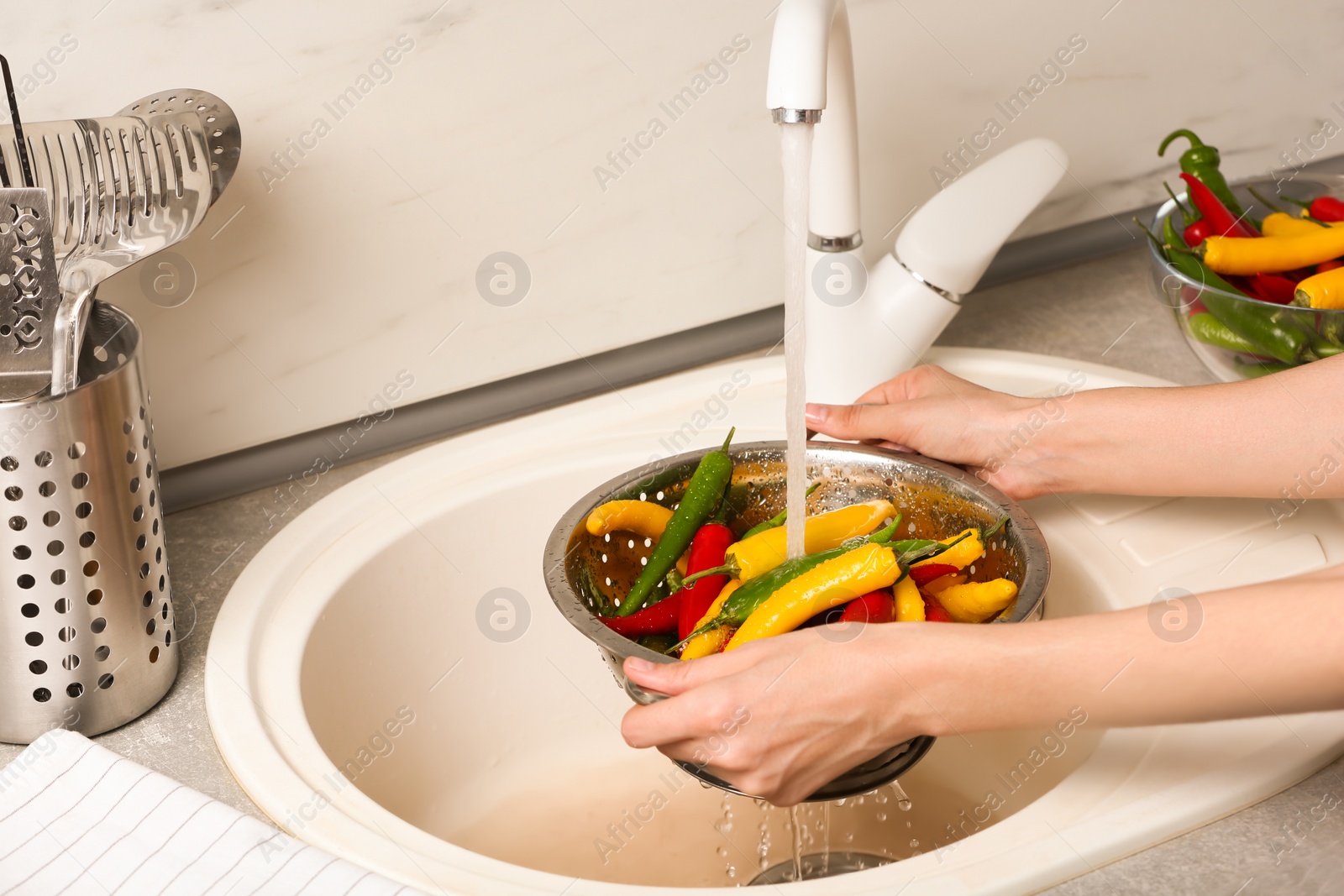 Photo of Woman washing chili peppers over sink, closeup