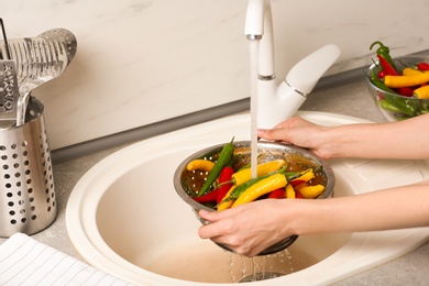 Woman washing chili peppers over sink, closeup