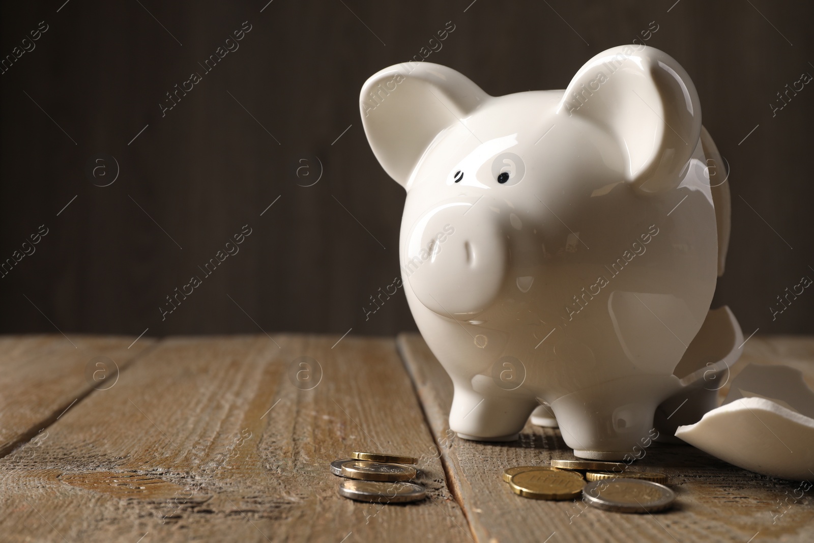 Photo of Poverty. Broken piggy bank and coins on wooden table, space for text