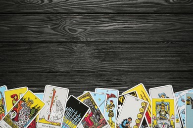 Photo of Tarot cards on black wooden table, top view. Space for text