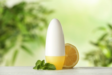 Photo of Deodorant container, mint and citrus on white wooden table against blurred background