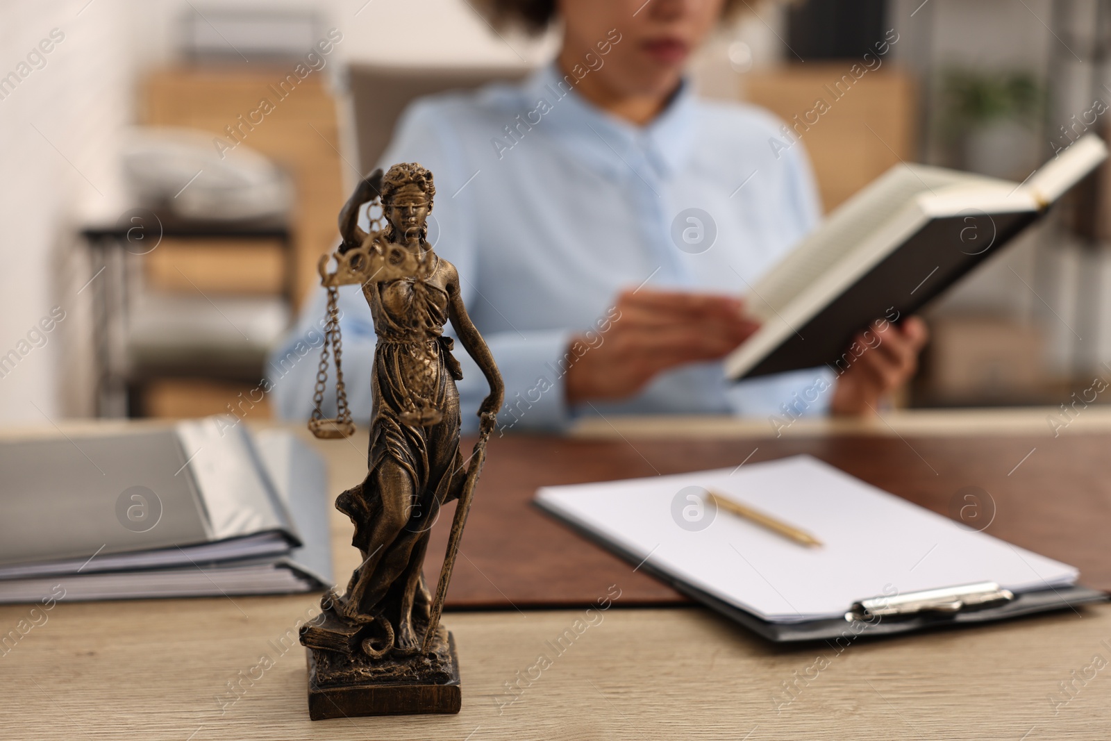 Photo of Notary with notebook at workplace in office, focus on statue of Lady Justice