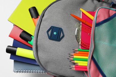 Backpack with different school stationery on white background, top view