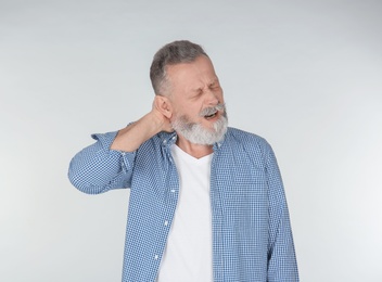 Man suffering from neck pain on light background