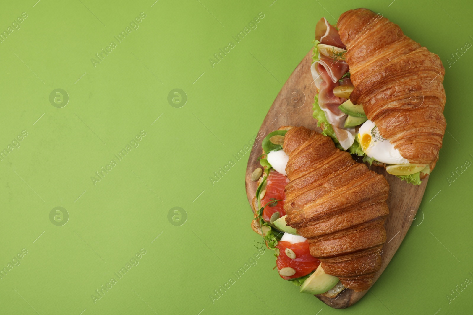 Photo of Delicious croissants with prosciutto and salmon on green table, top view. Space for text