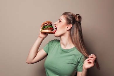 Pretty woman eating tasty burger on color background. Space for text