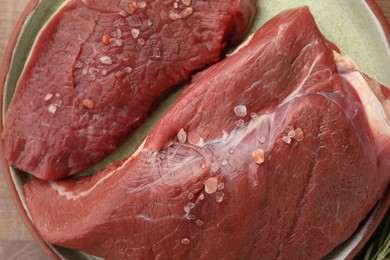 Photo of Pieces of raw beef meat with spices on plate, top view