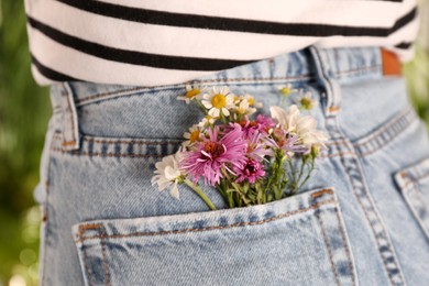 Photo of Woman with beautiful tender flowers in back pocket of jeans outdoors, closeup