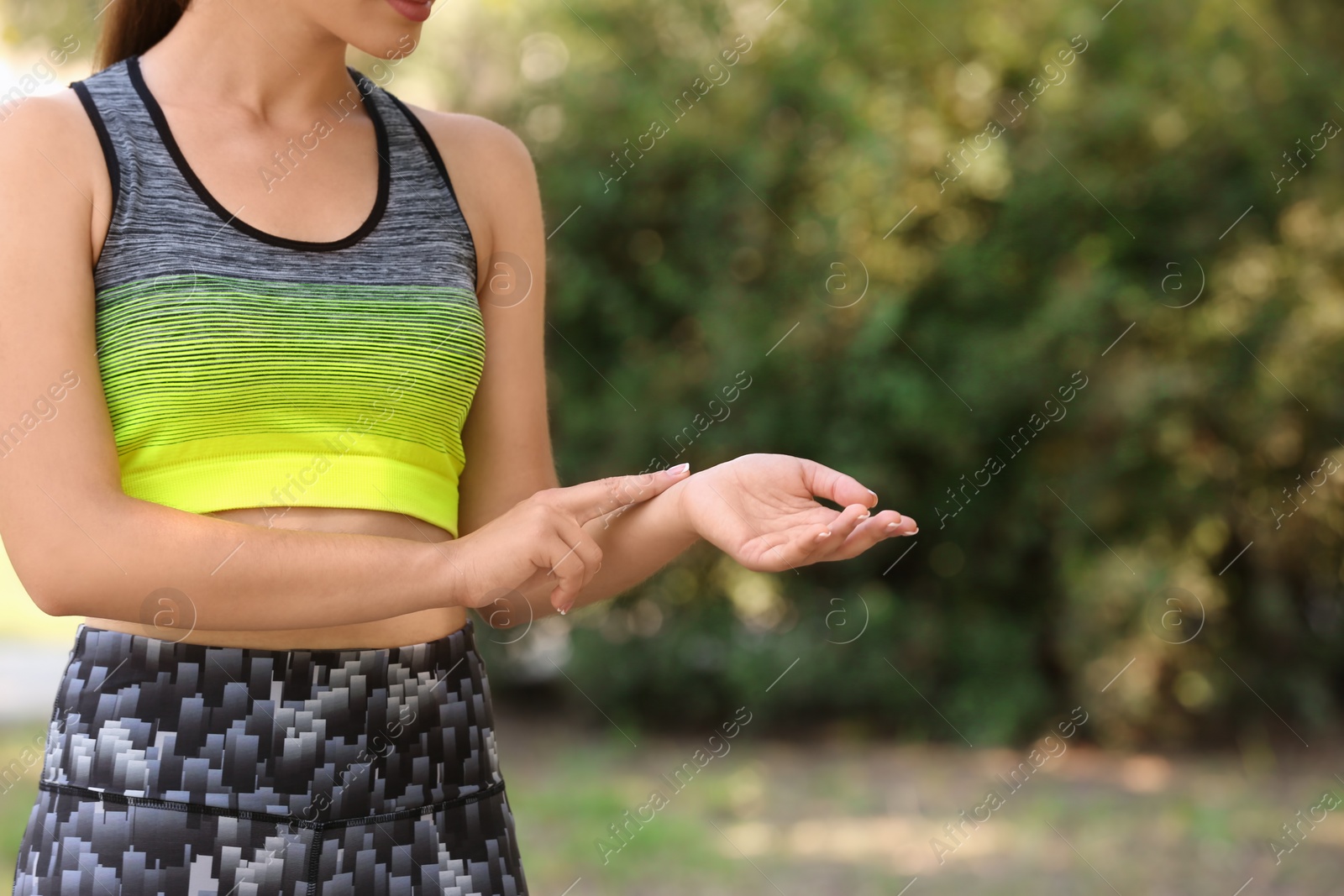 Photo of Young woman checking pulse outdoors on sunny day