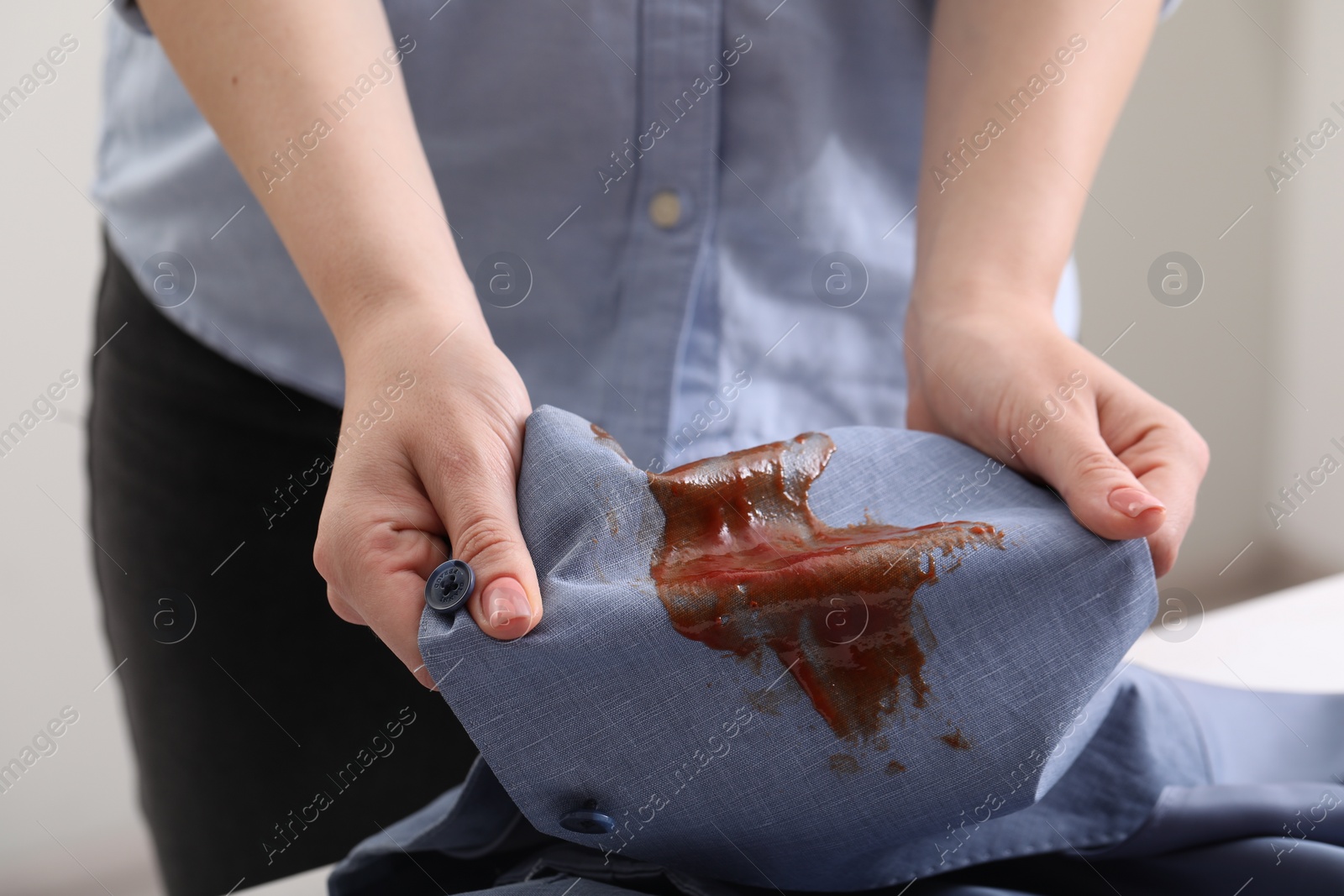 Photo of Woman holding shirt with stain of sauce on blurred background, closeup