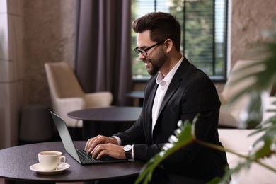 Photo of Happy young man with glasses working on laptop at table in office