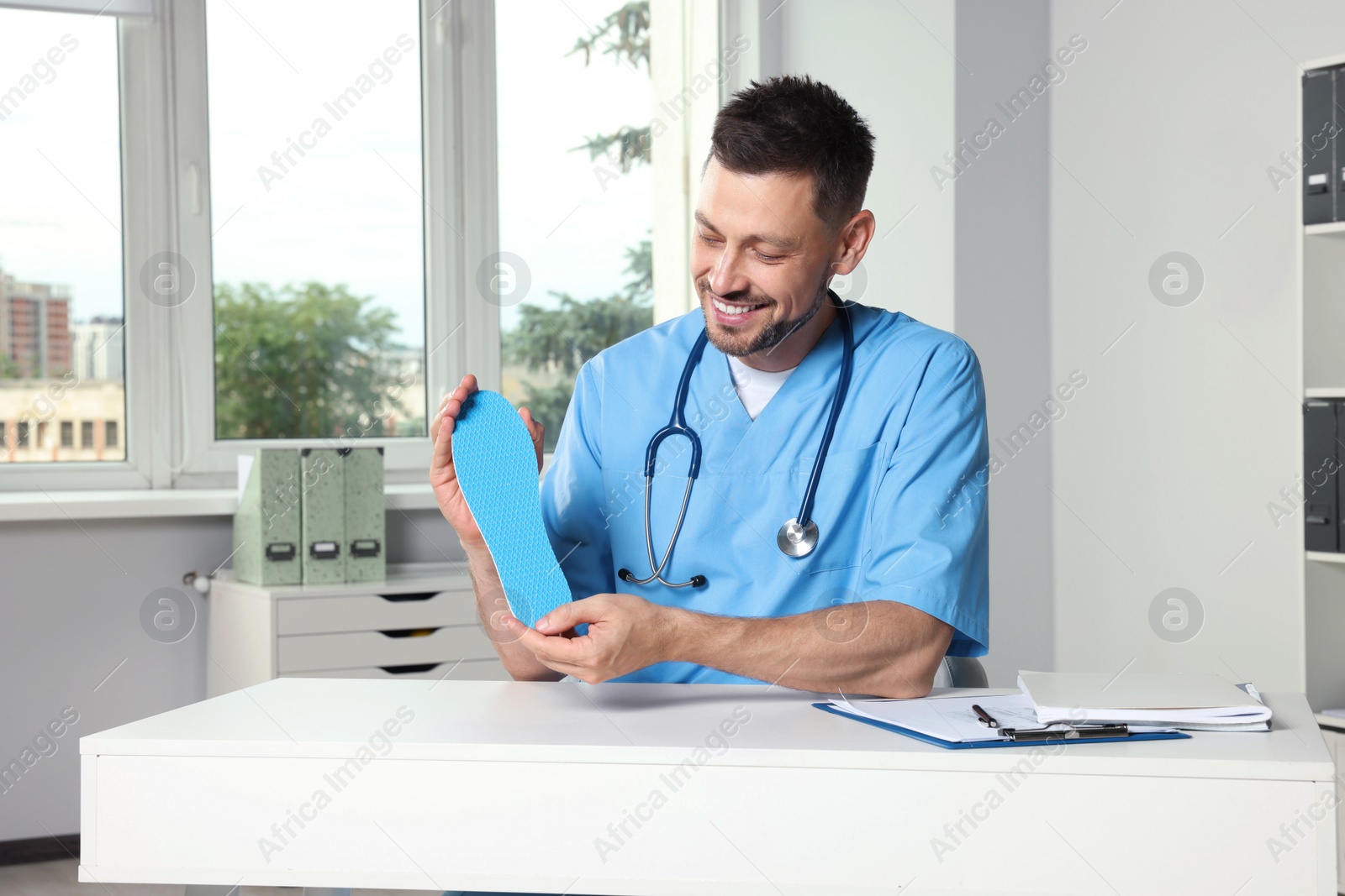 Photo of Handsome male orthopedist showing insole in hospital