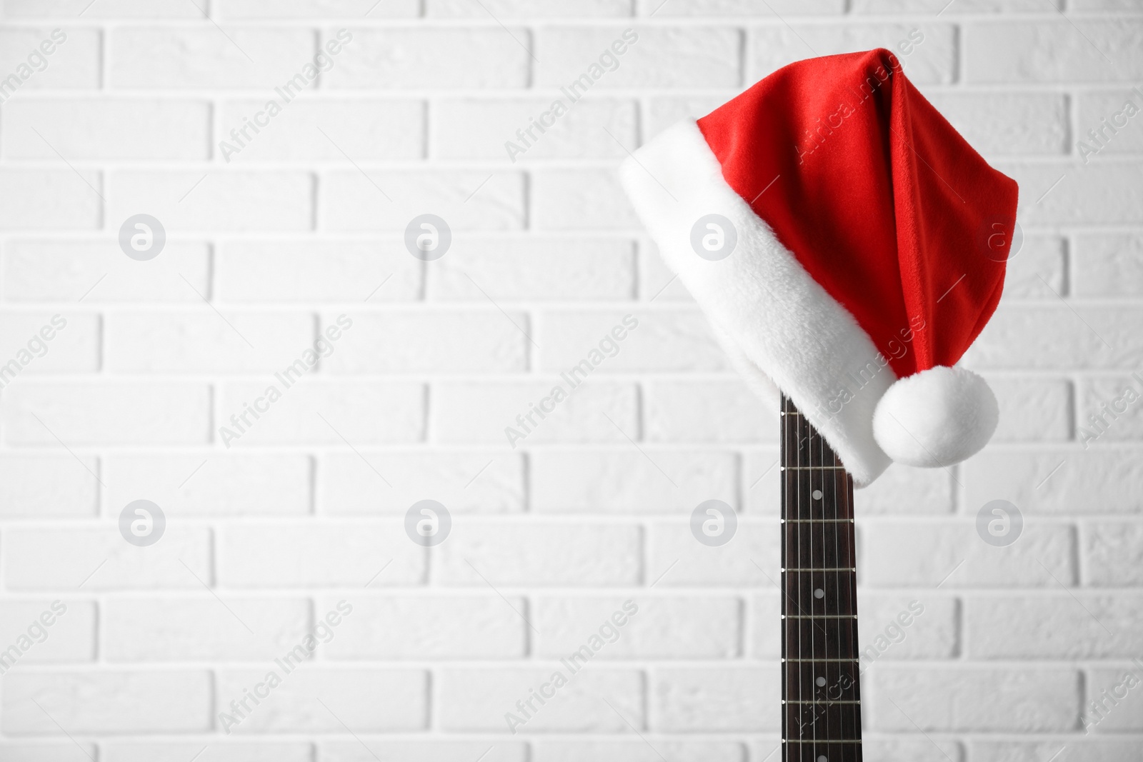 Photo of Guitar with Santa hat against white brick wall, space for text. Christmas music