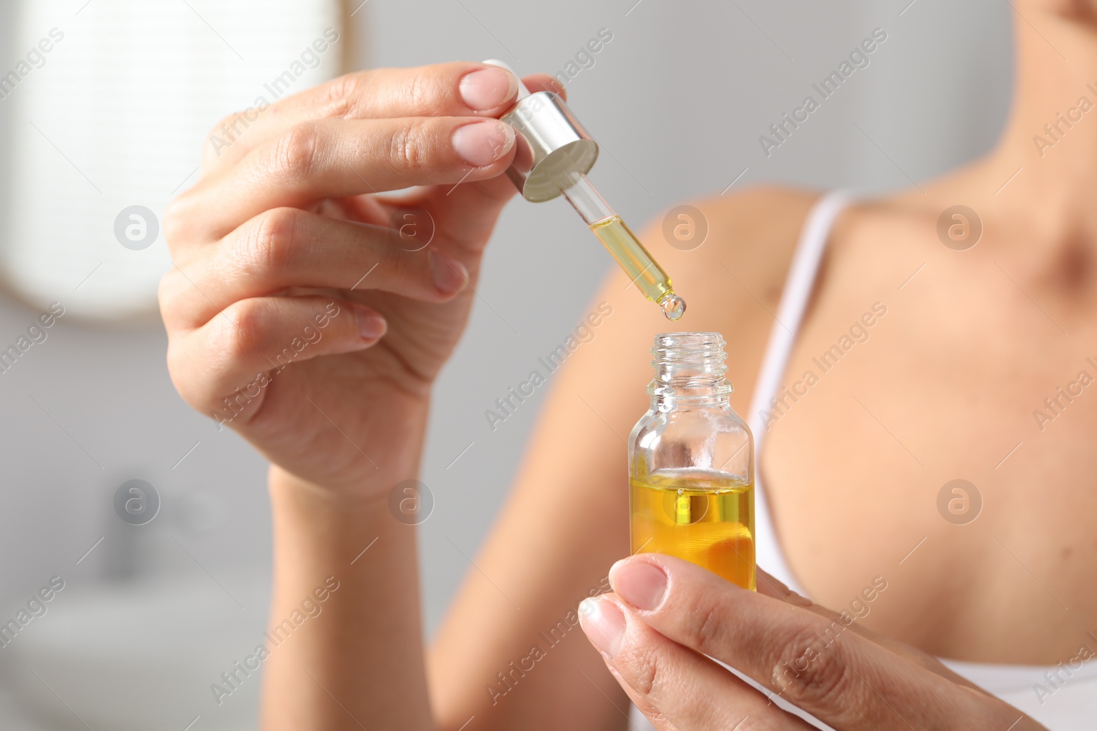 Photo of Woman with bottle of cosmetic serum on blurred background, closeup