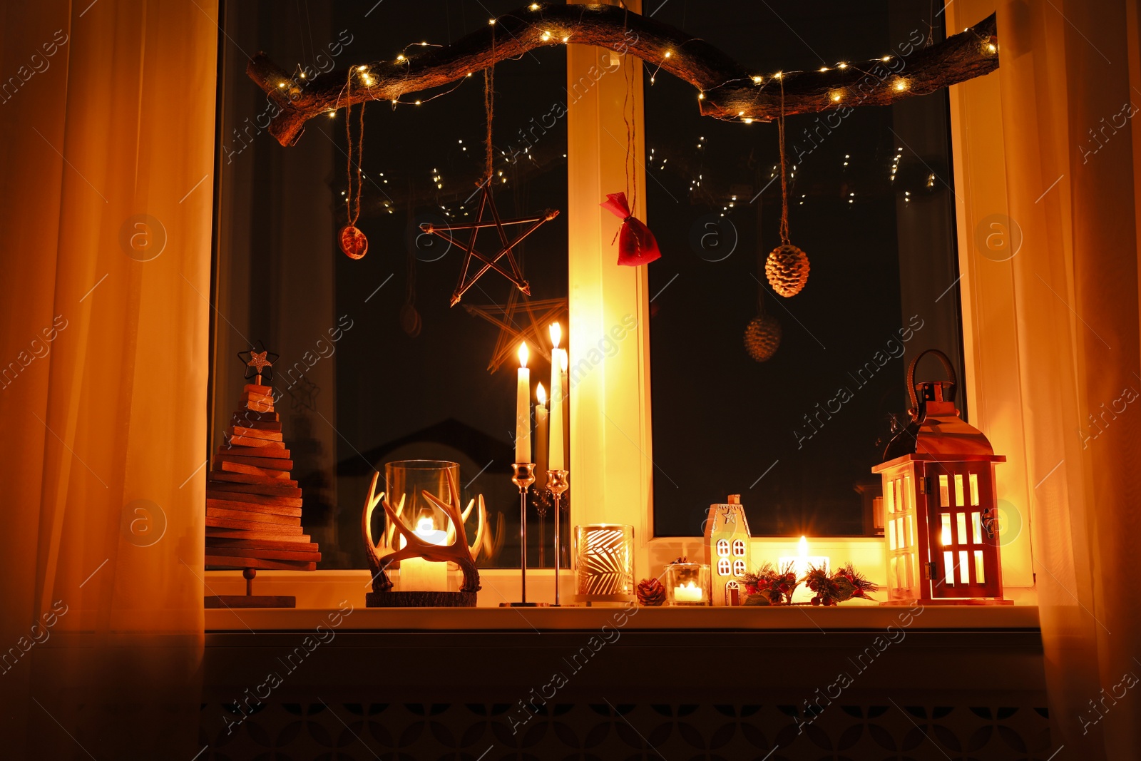 Photo of Burning candles and Christmas decor on window sill at night