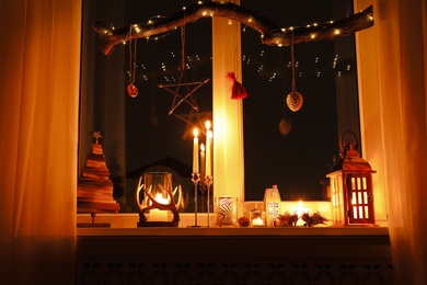 Burning candles and Christmas decor on window sill at night