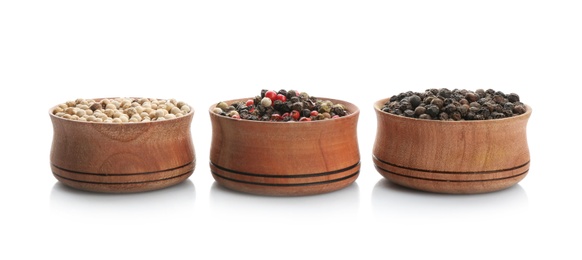 Bowls with different kinds of pepper grains on white background