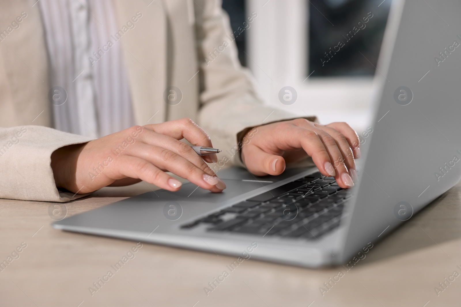 Photo of Woman with pen working on laptop at wooden table, closeup. Electronic document management