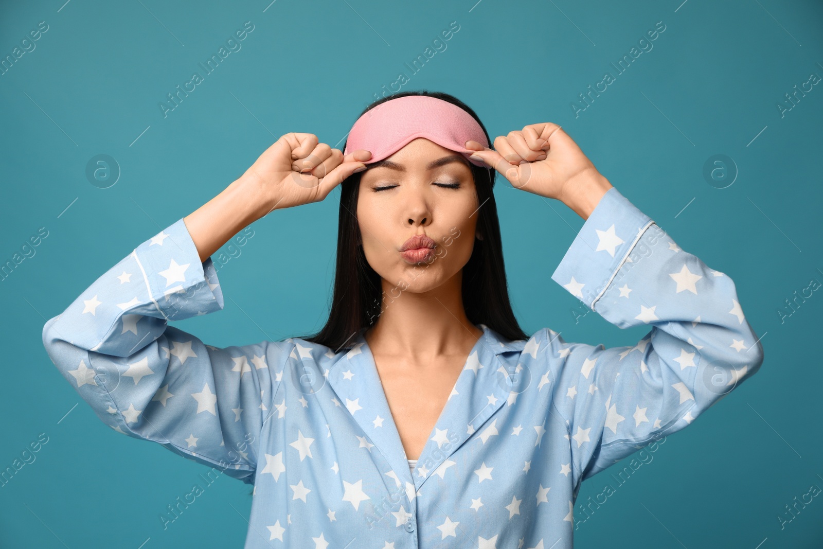 Photo of Beautiful Asian woman wearing pajamas and sleeping mask on blue background. Bedtime