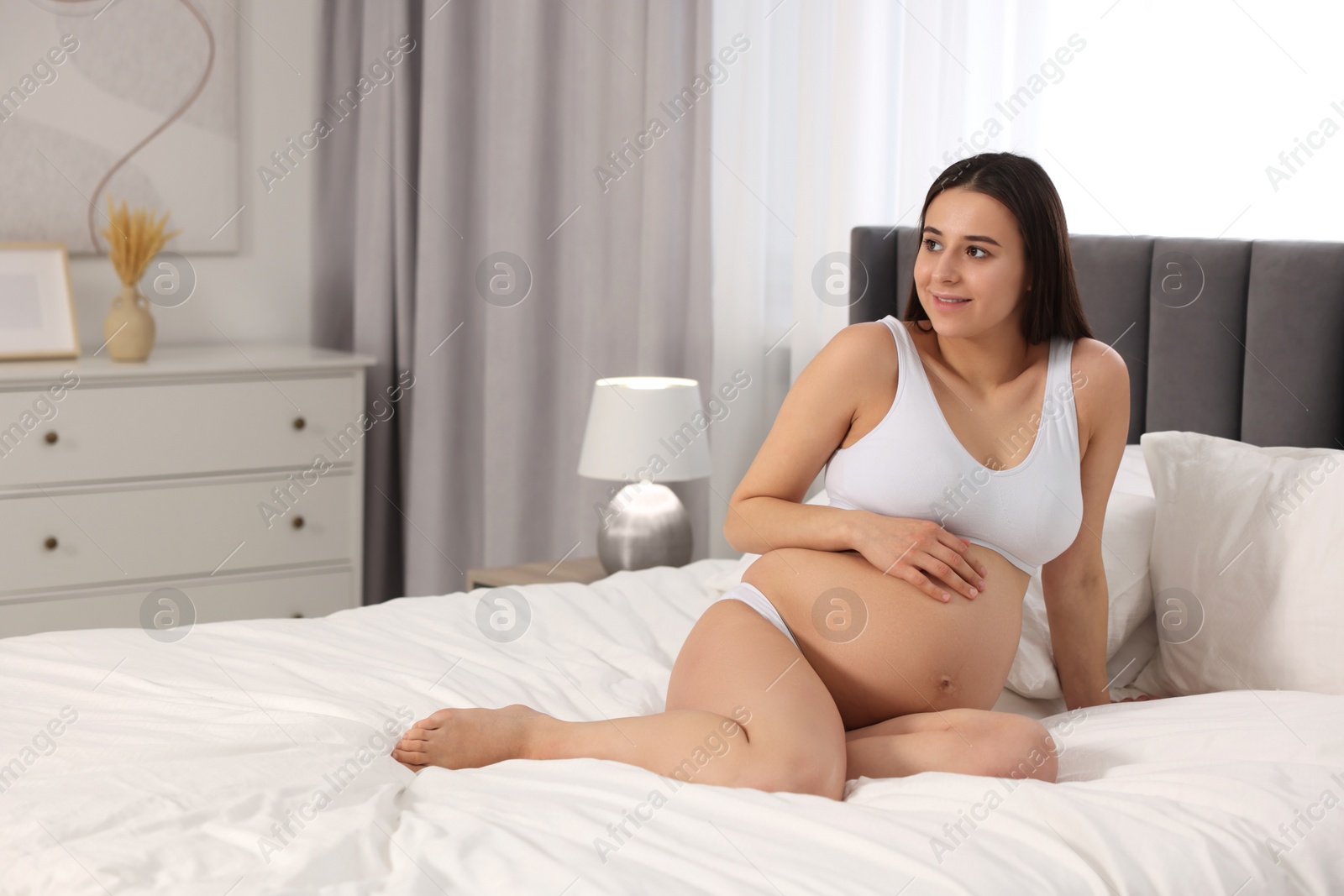Photo of Beautiful pregnant woman in stylish comfortable underwear on bed at home, space for text