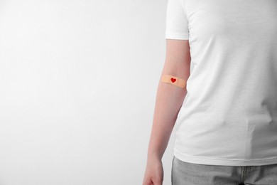 Blood donation concept. Woman with adhesive plaster on arm against white background, closeup. Space for text