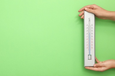 Woman with weather thermometer on green background, closeup. Space for text
