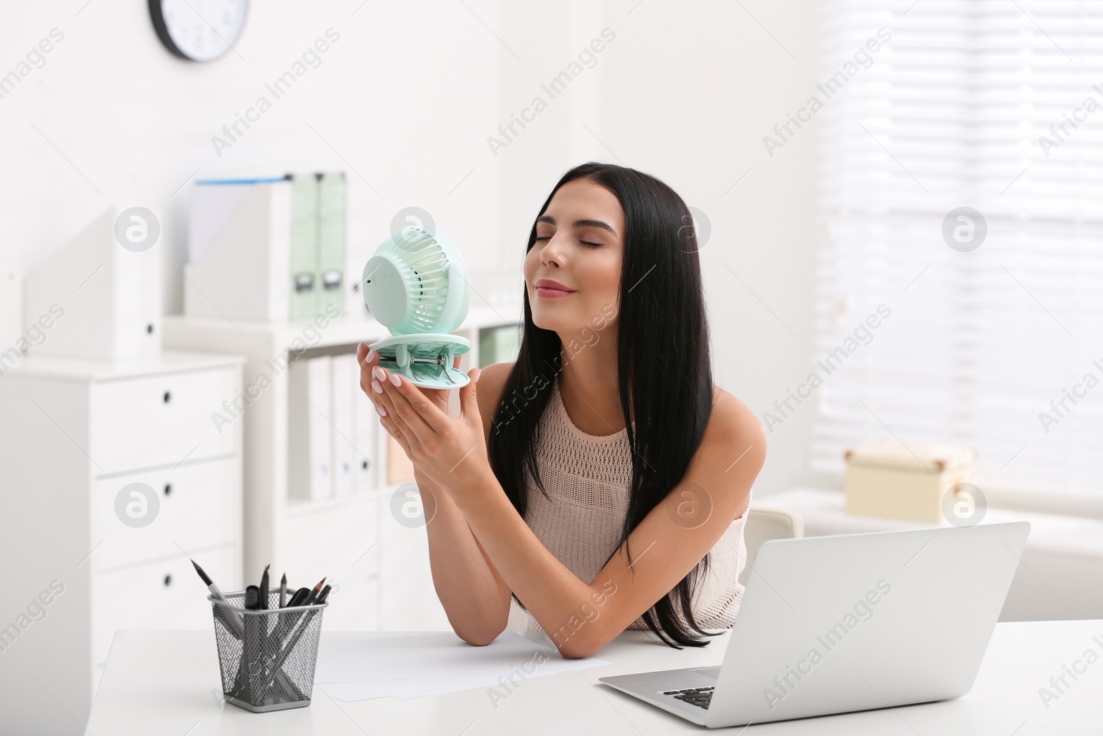 Photo of Young woman enjoying air flow from fan at workplace