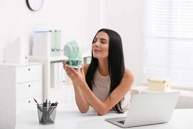 Young woman enjoying air flow from fan at workplace