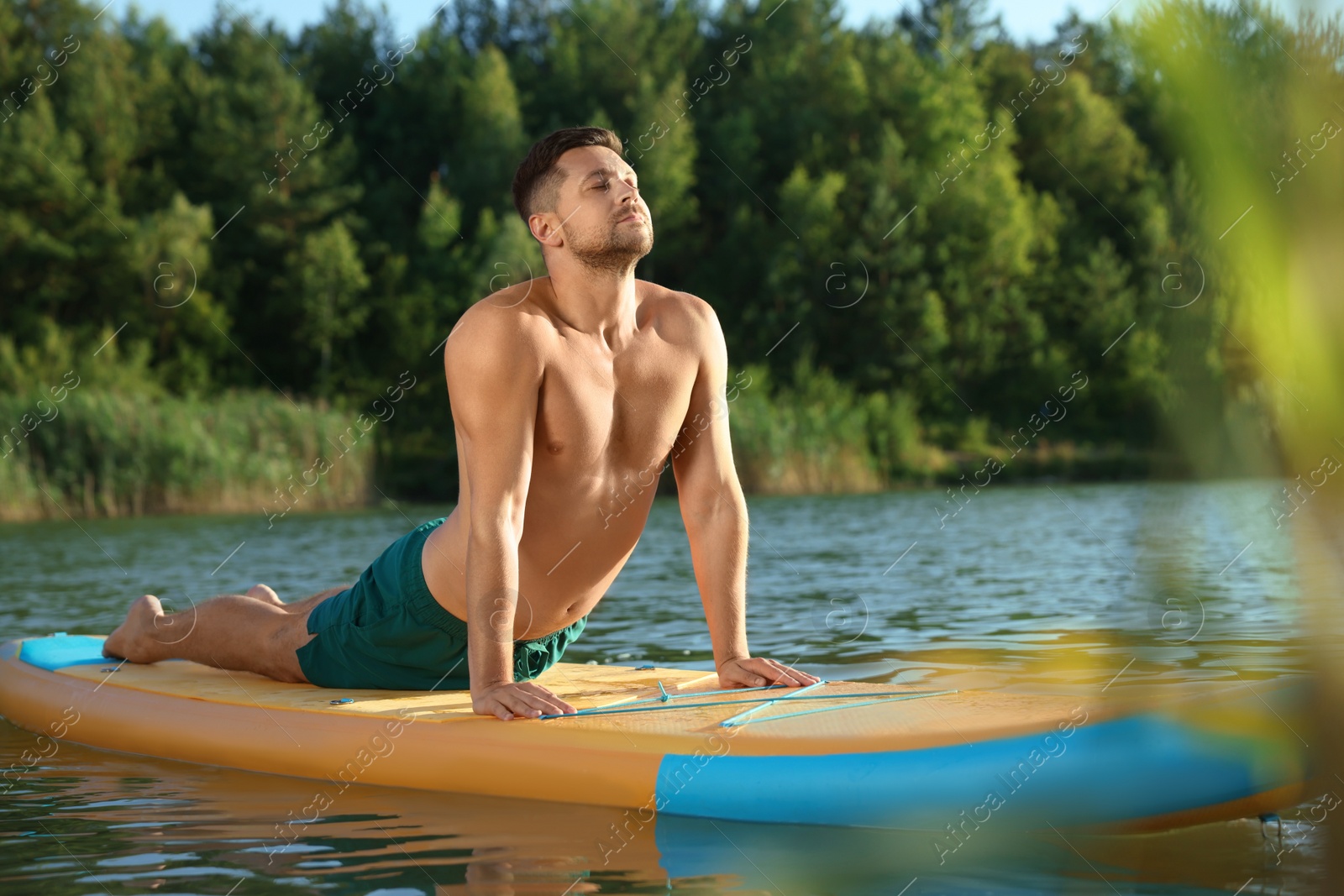 Photo of Man practicing yoga on color SUP board on river