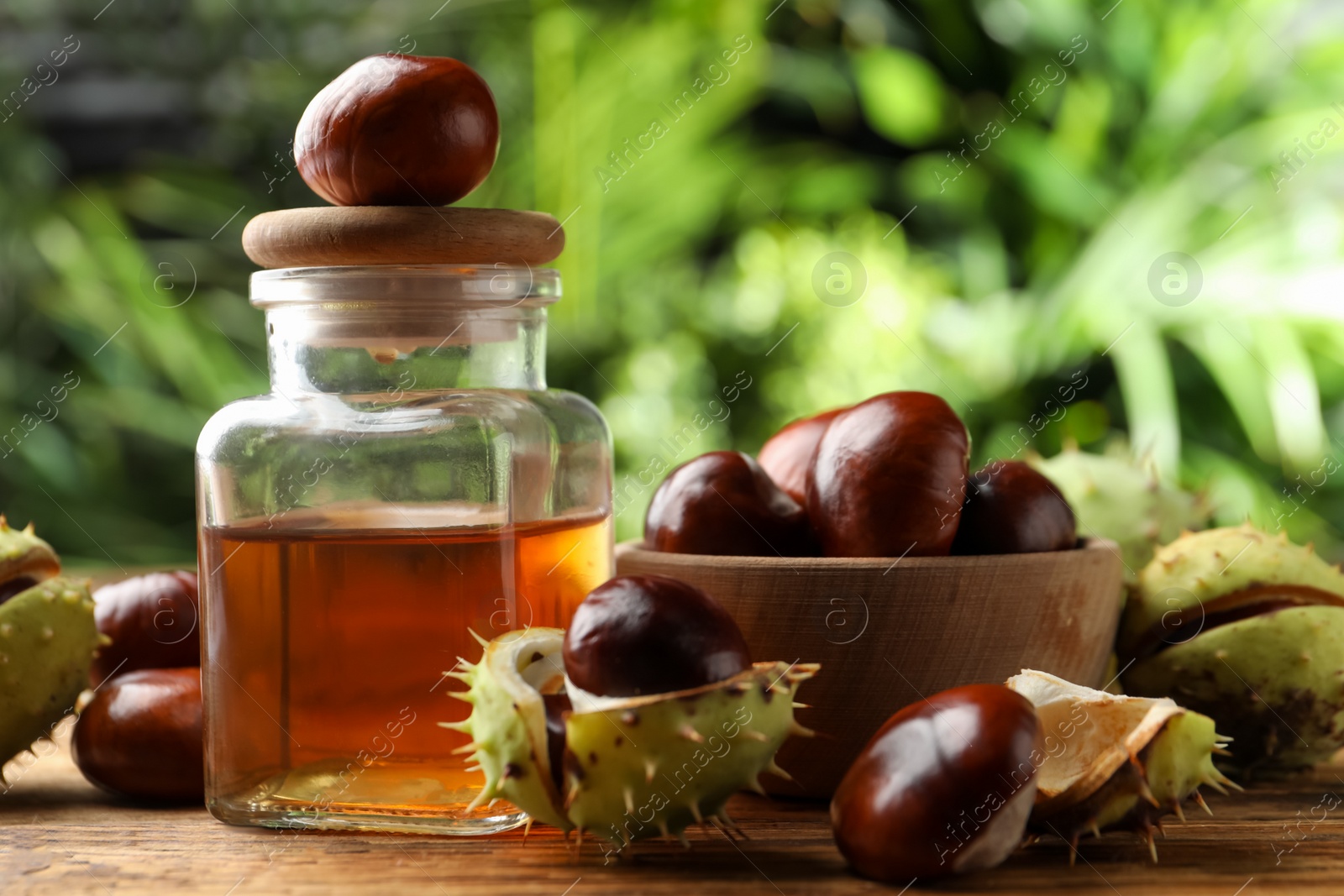 Photo of Chestnuts and jar of essential oil on table against blurred background