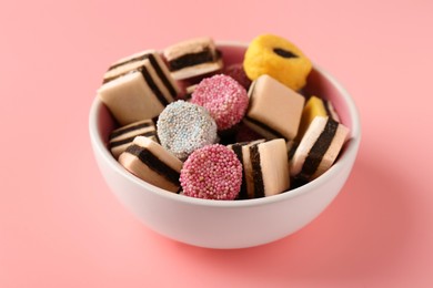 Bowl of tasty liquorice candies on pink background