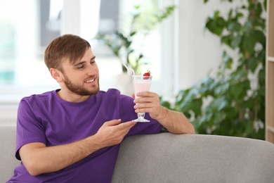 Photo of Young man with glass of delicious milk shake indoors