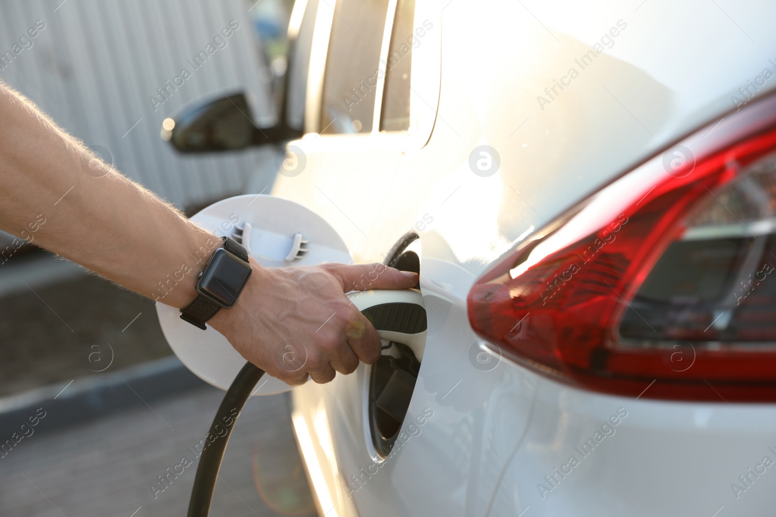 Photo of Man inserting plug into electric car socket at charging station, closeup