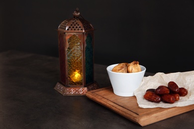 Photo of Muslim lantern Fanous and dried fruits on table against dark background